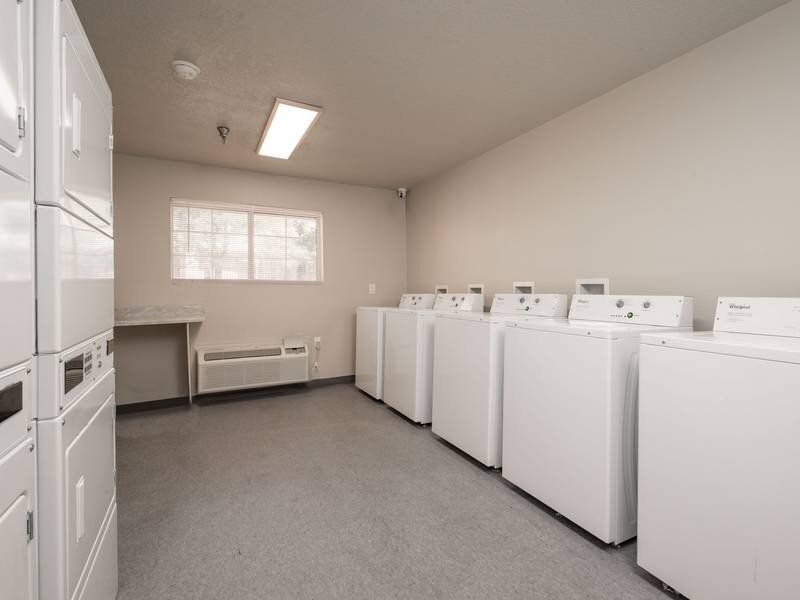 Laundry room with a row of white front-loading washers and dryers along the wall at Santa Fe Suites in Santa Fe, NM.
