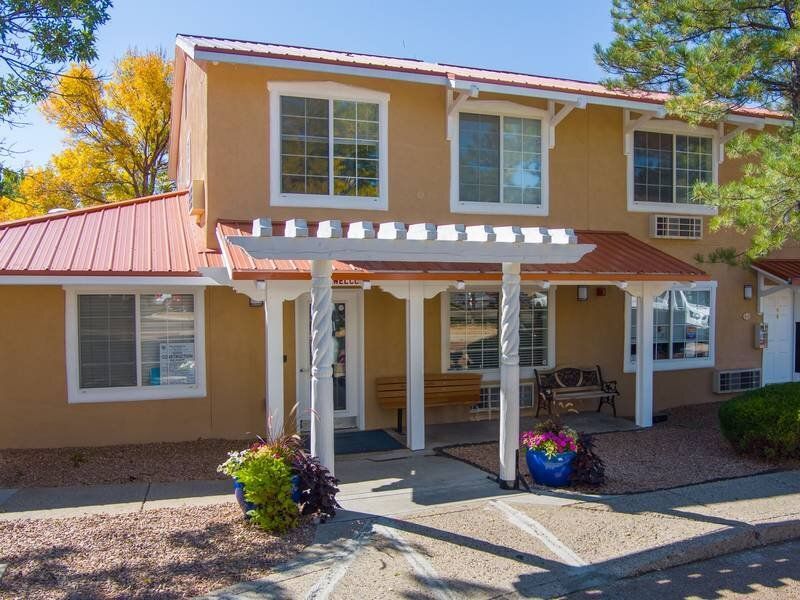 Two-story beige apartment building exterior with a covered entrance and benches at Santa Fe Suites in Santa Fe, NM.