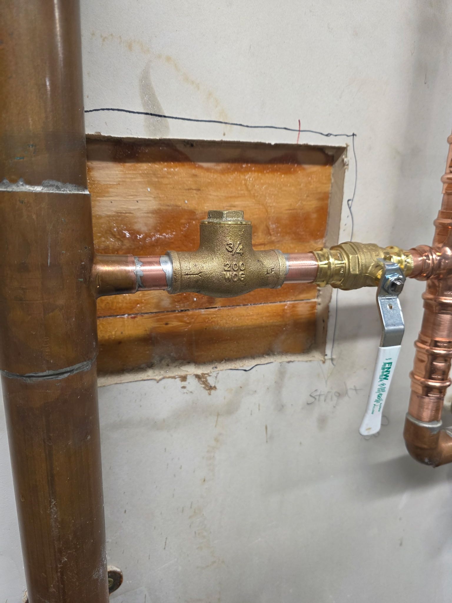 Copper plumbing with a brass tee, shut-off valve, and exposed wooden wall.