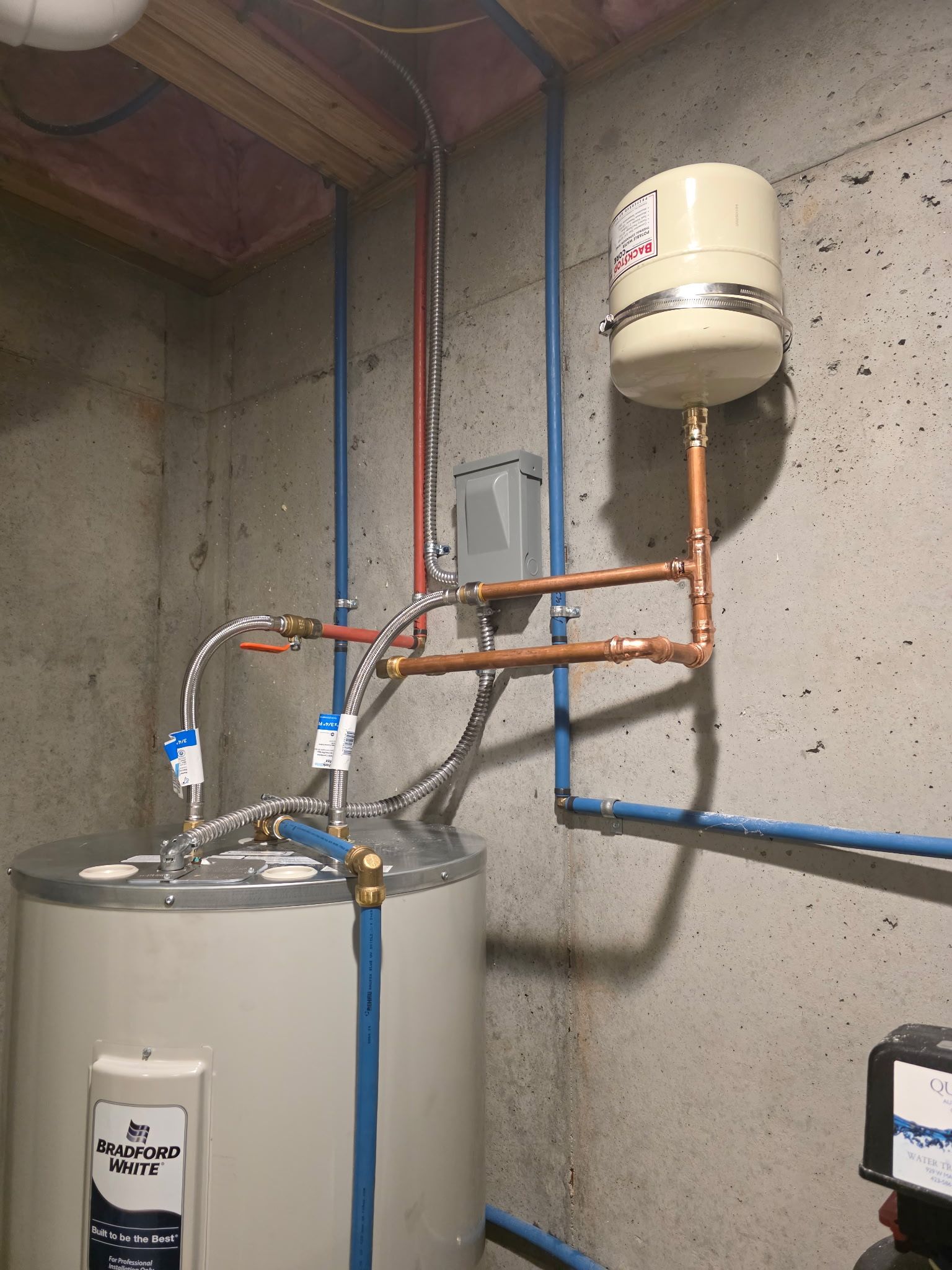Water heater with attached expansion tank and blue and copper pipes in a basement.
