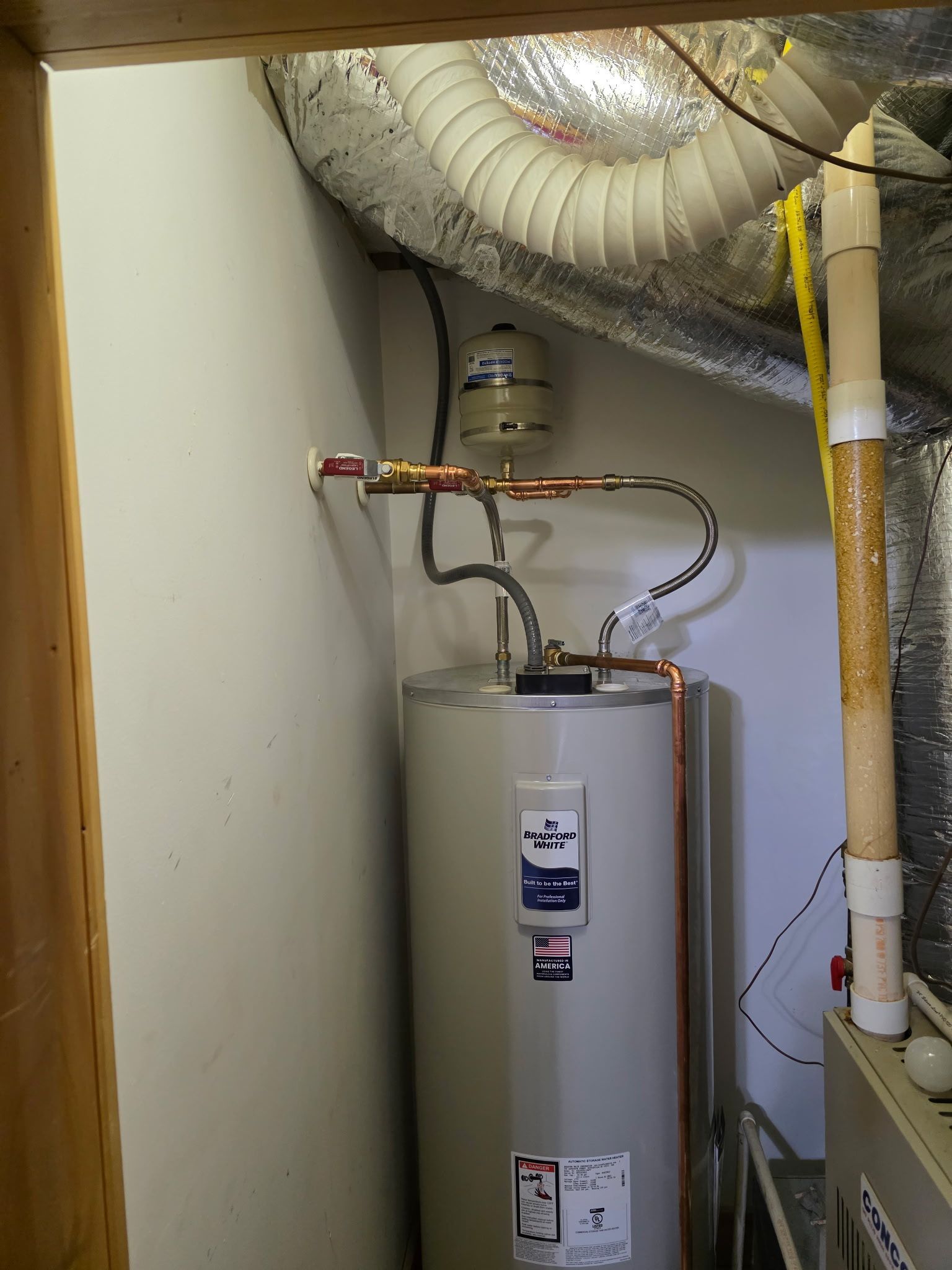 Water heater in a utility room, with copper pipes and a connected expansion tank.