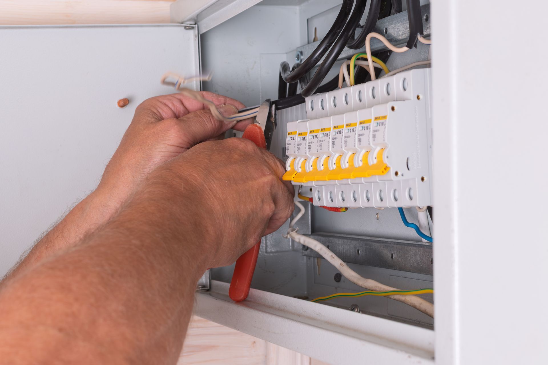 An electrician uses side cutters to trim and organize wires inside a fuse box An electrician uses side cutters to trim and organize wires inside a fuse box