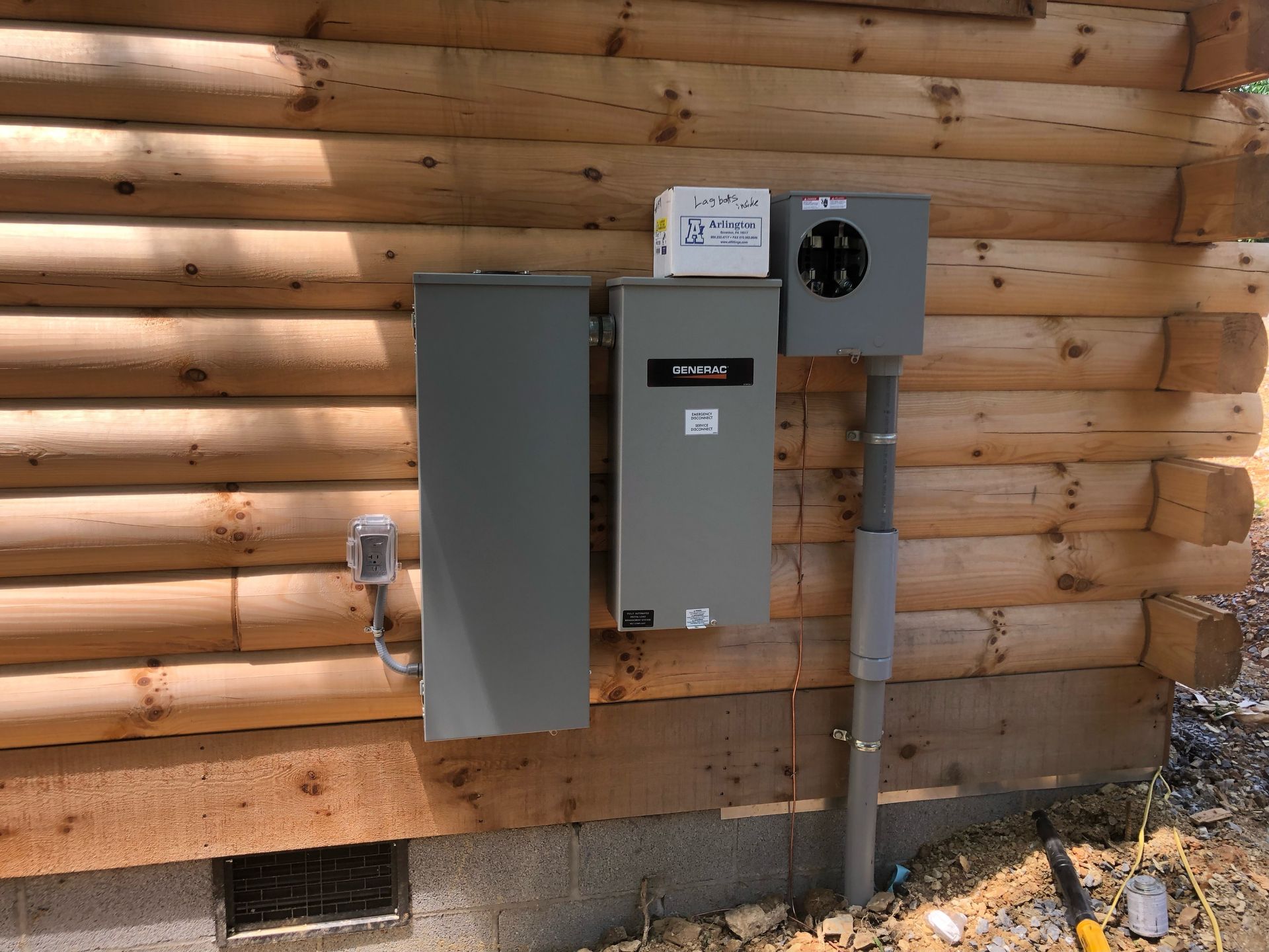 Electrical panel boxes mounted on a log cabin exterior. Gray boxes, conduit, and meter socket.
