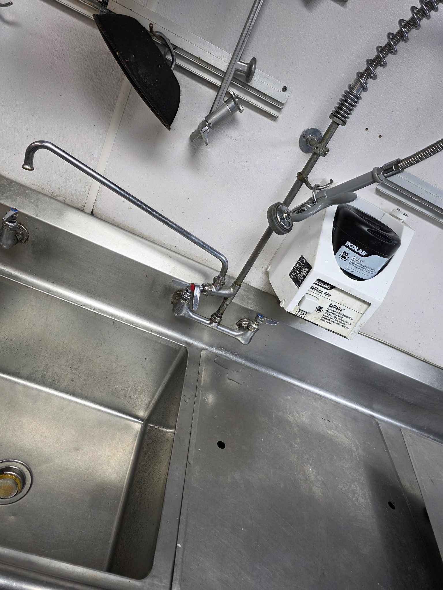 Stainless steel commercial sink with a faucet, and a white water heater mounted above.
