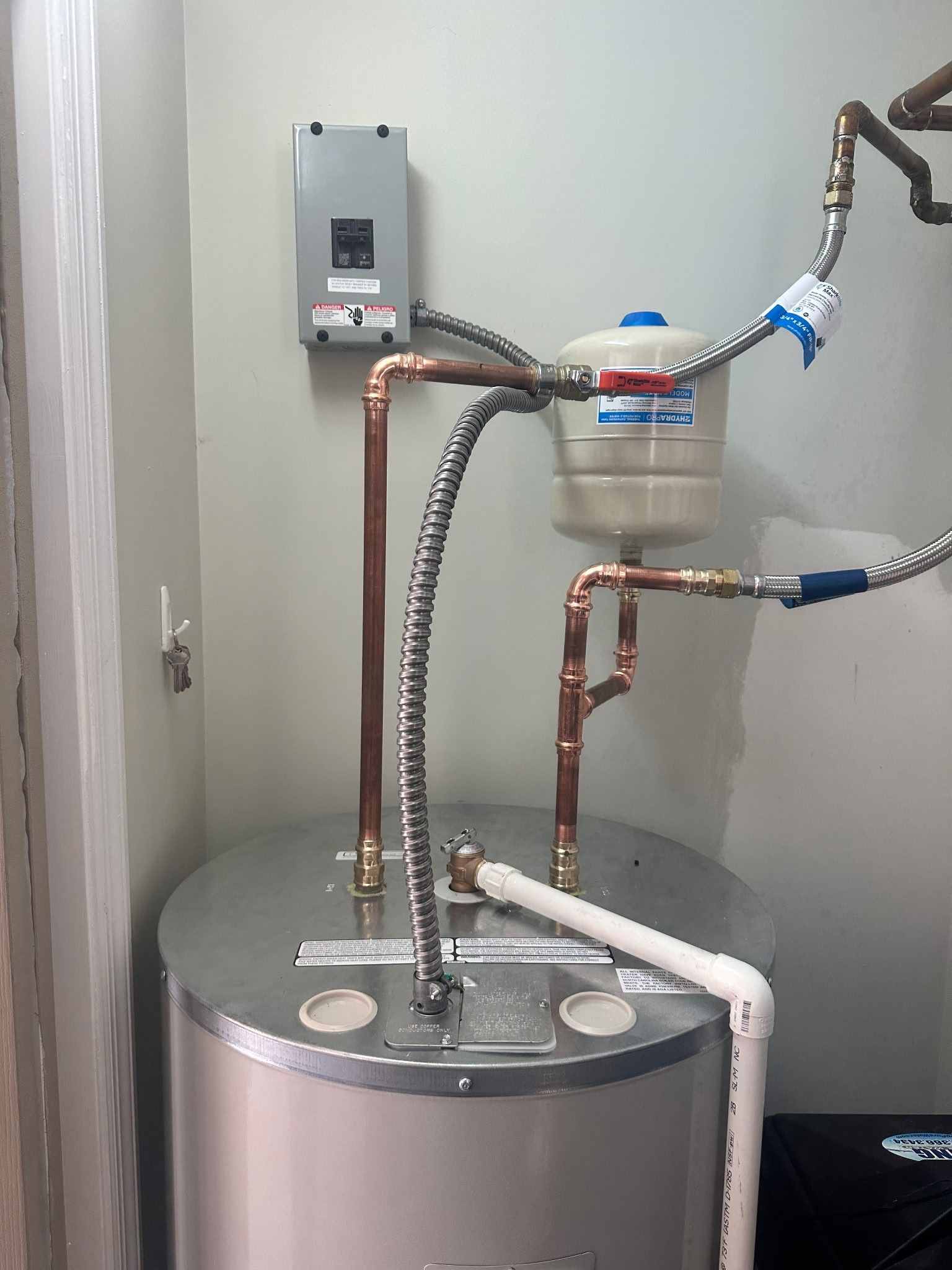 Water heater with copper pipes and pressure tank against a light green wall.