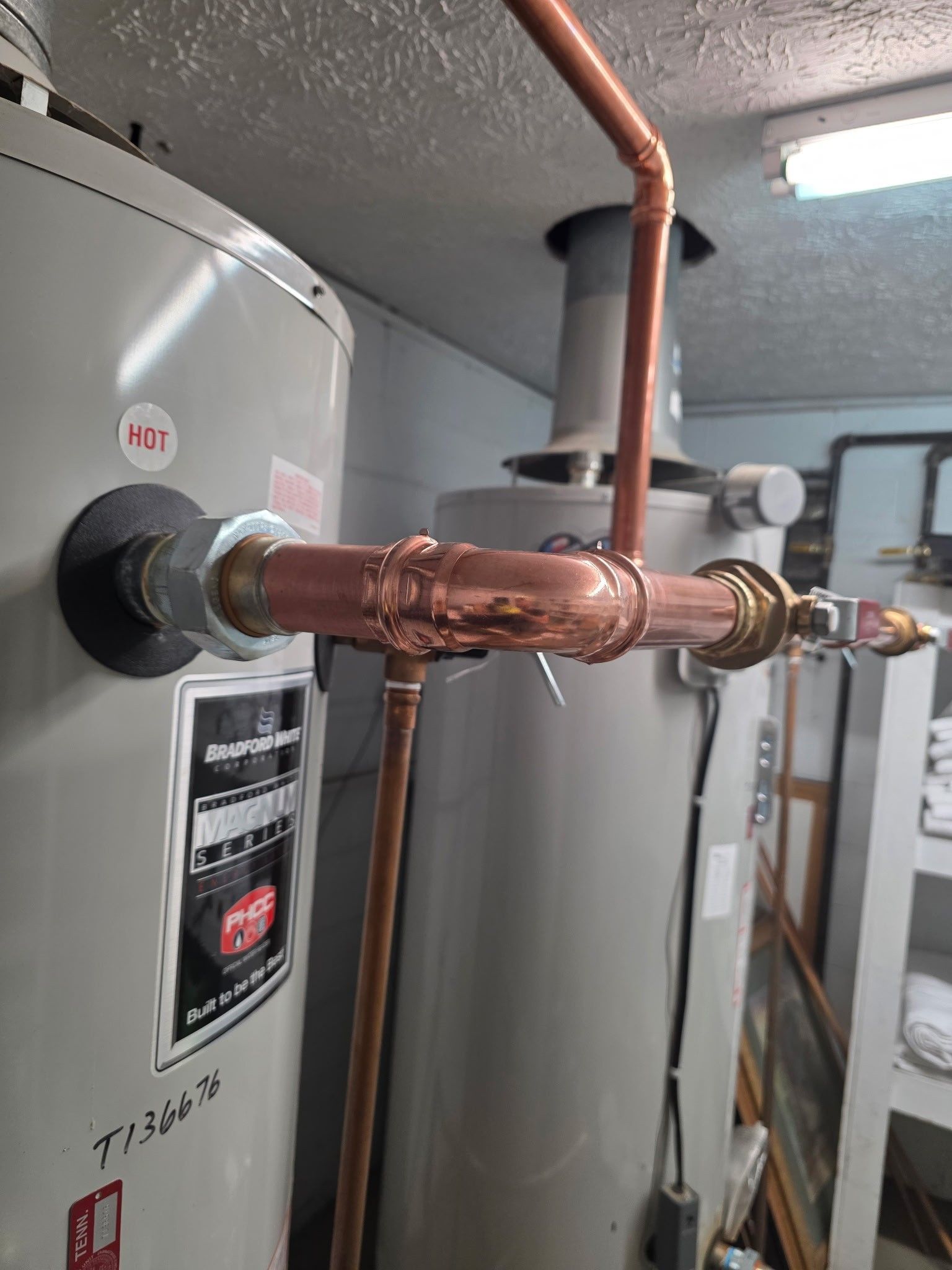 Copper pipes connected to two water heaters in a utility room.