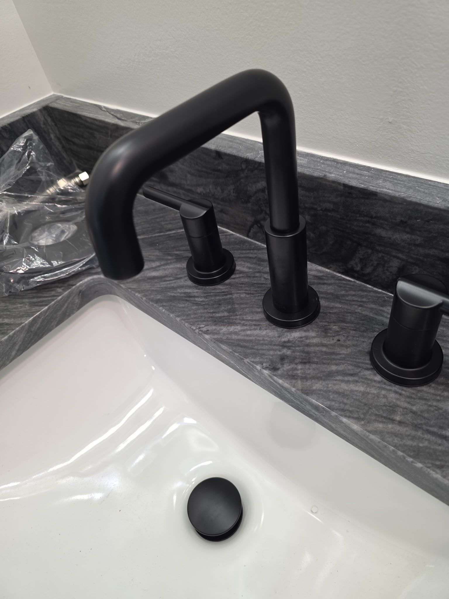 Matte black bathroom faucet on gray countertop over white sink.