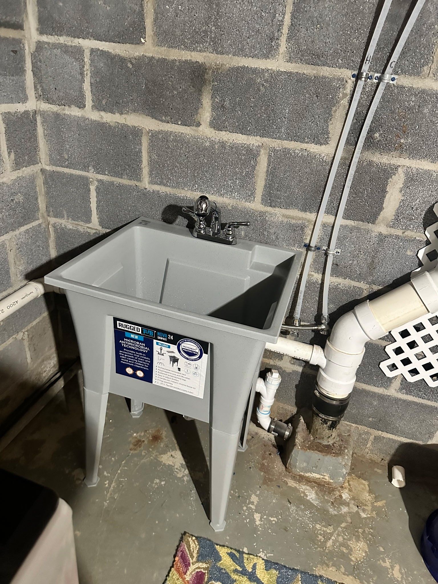 A gray utility sink with chrome faucet and plumbing in a basement with cinder block walls.