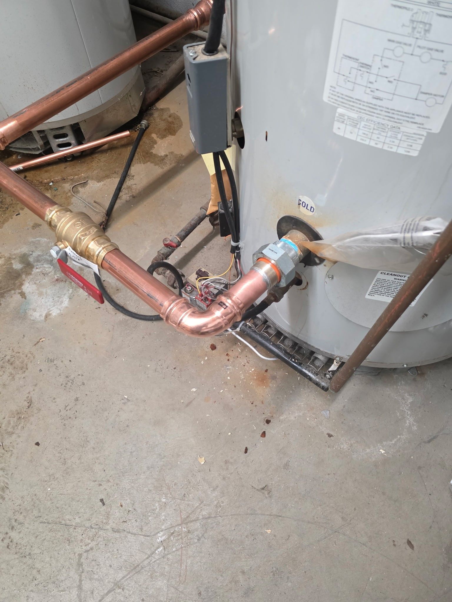 Copper pipes and fittings connected to a water heater in a concrete-floored utility space.