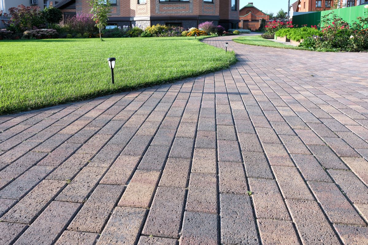 Brick pathway meandering through vibrant green lawns, leading to a row of commercial establishments.