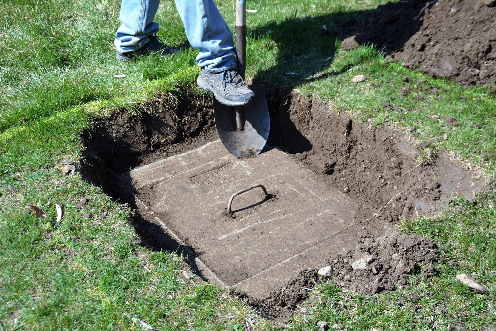 Technician excavating a residential yard to access a septic tank before performing repairs.