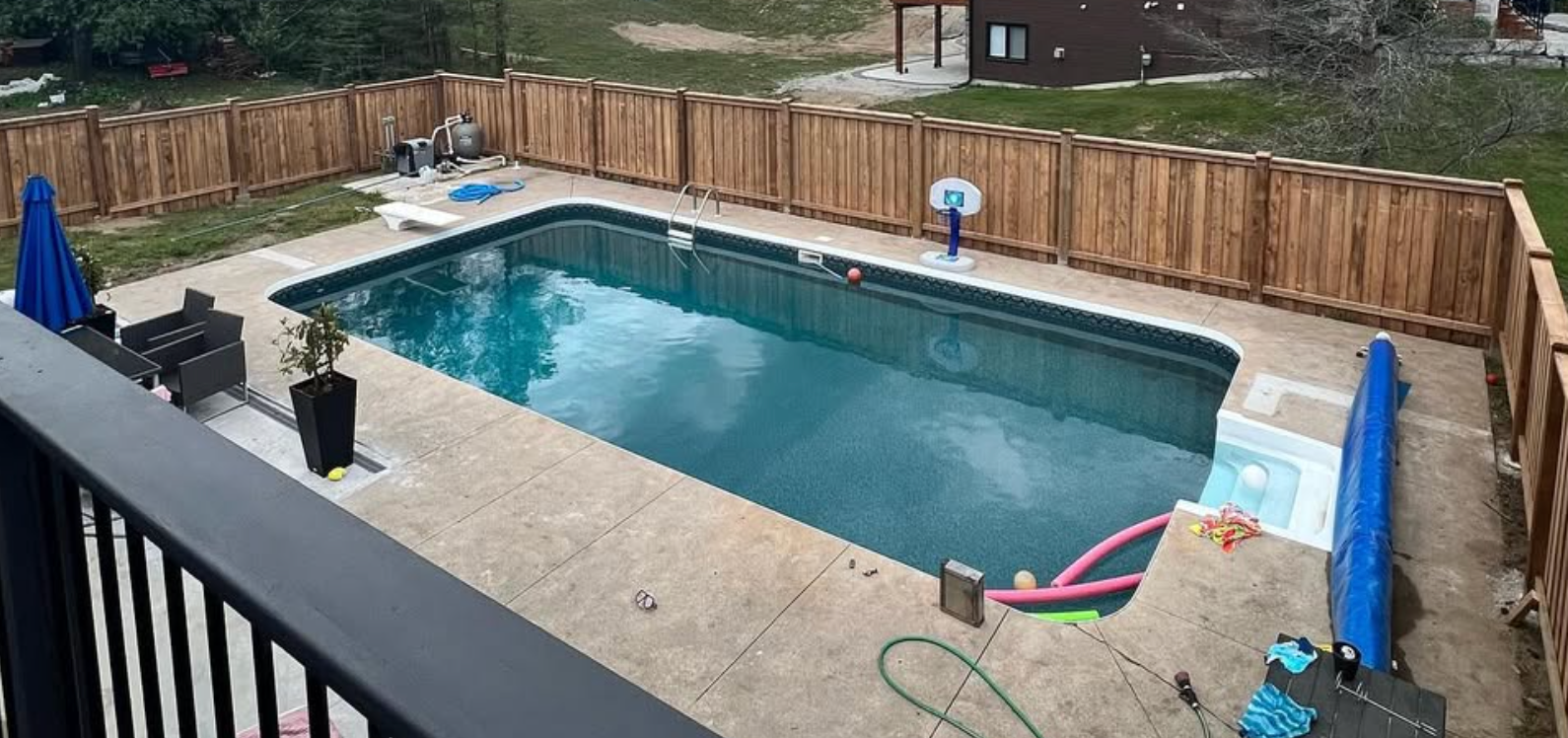 Backyard swimming pool surrounded by a wooden fence, with a deck and patio furniture.