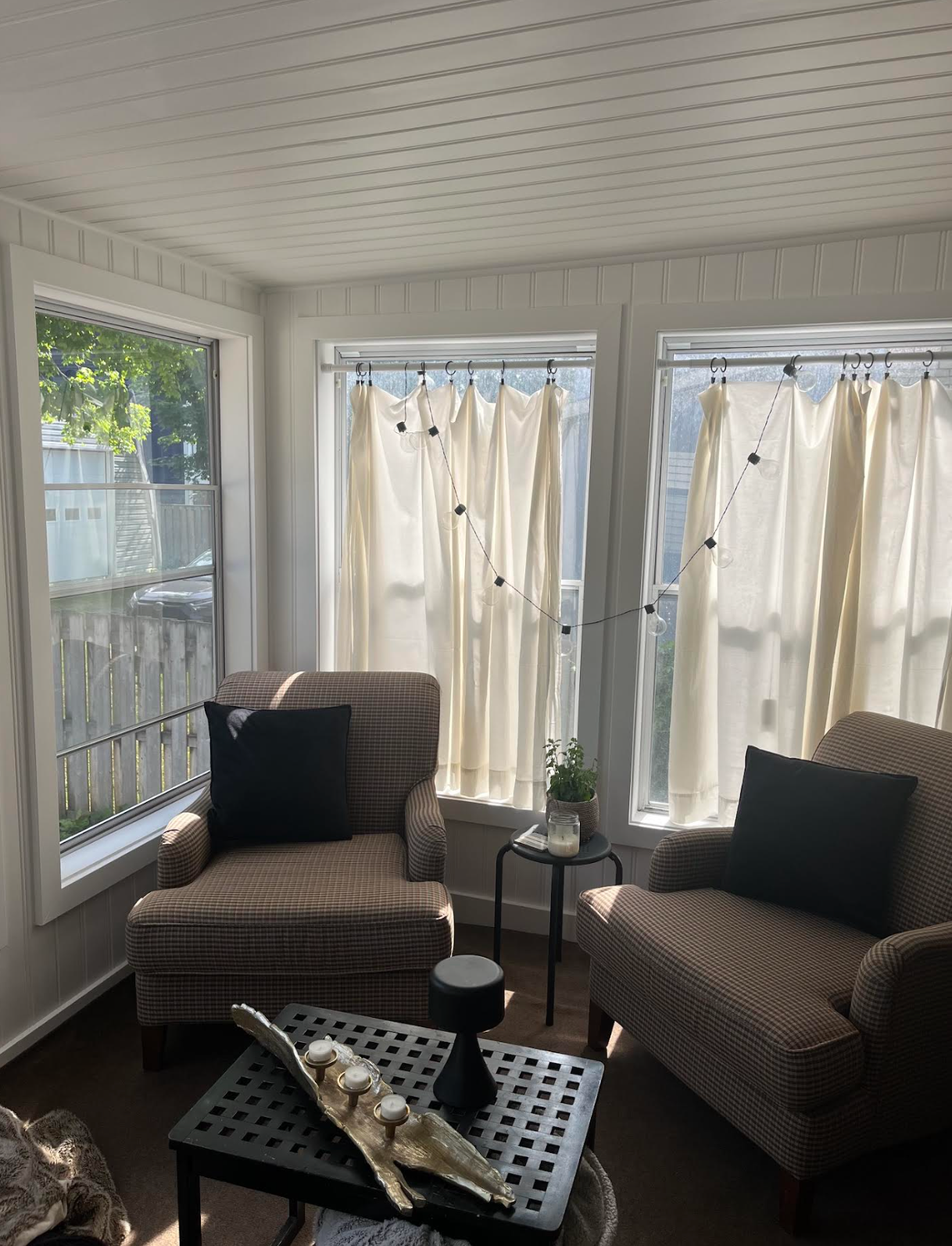 Sunroom with two wicker chairs, small table, and white curtains by large windows