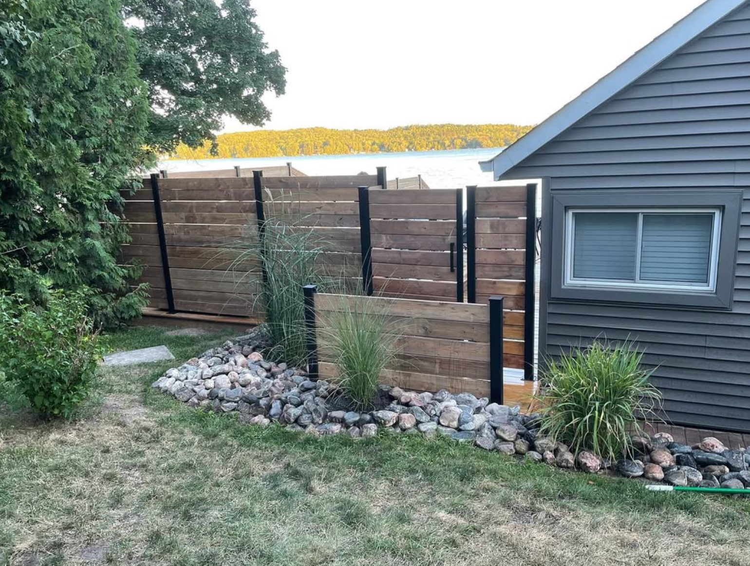 Backyard fence with wood panels, rocks, and plants beside a gray house exterior