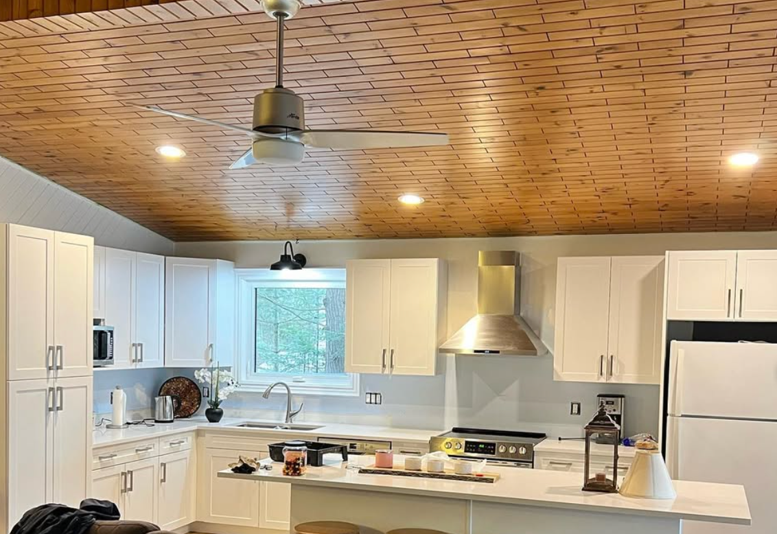 Bright kitchen with white cabinets, wood ceiling, island counter, and ceiling fan.