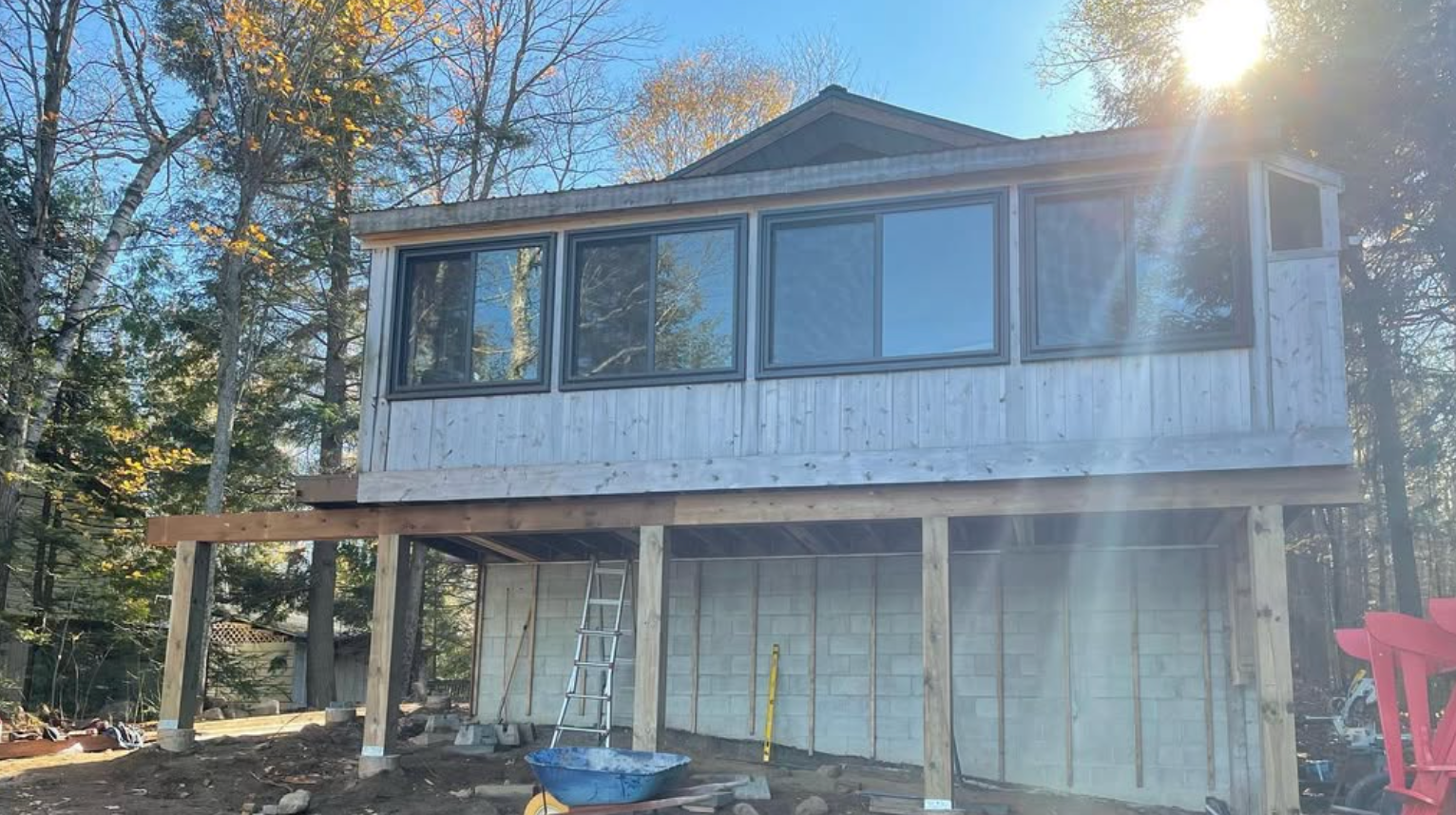 Partially renovated two-story house with a wooden deck and bright sun glare in a wooded yard