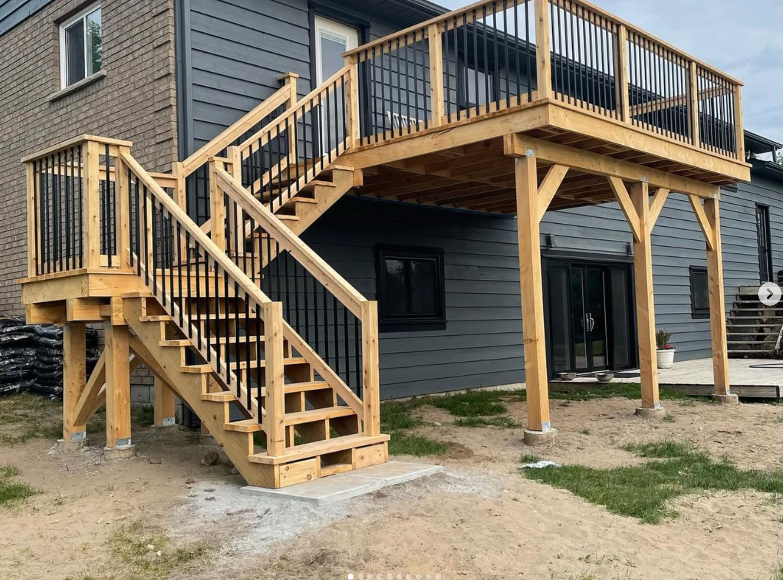 Wooden elevated deck and staircase attached to a gray house with black railings and posts.