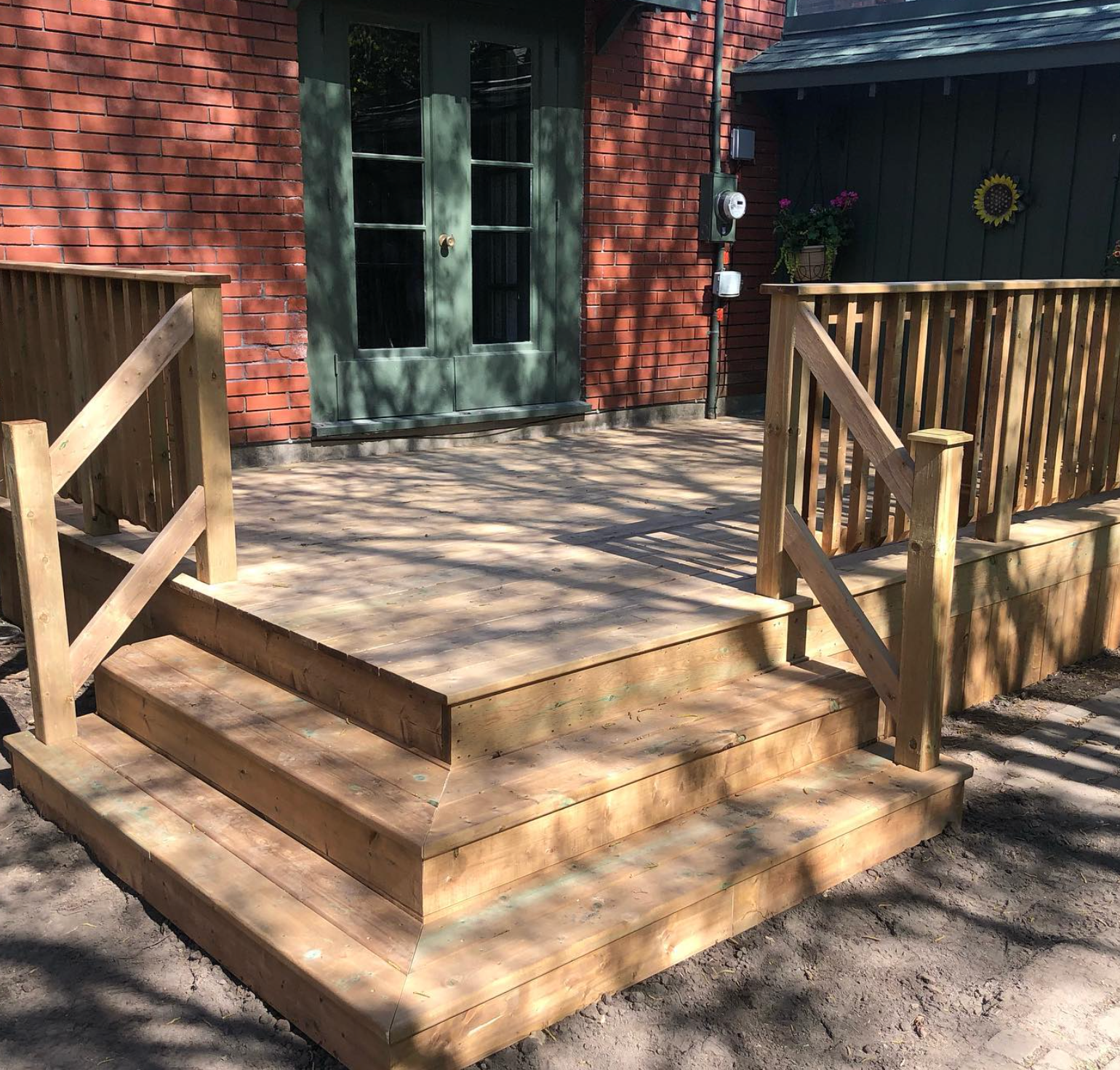 Wooden porch steps with railings leading to green double doors on a red brick house.