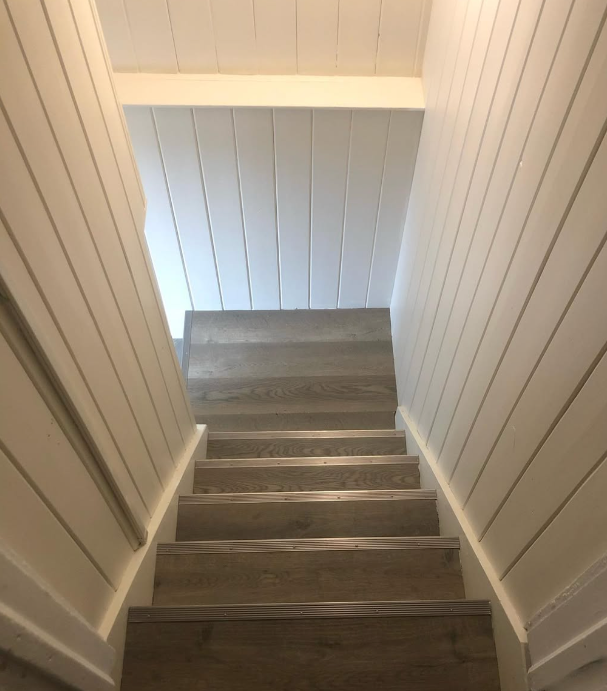 Narrow carpeted staircase with white paneled walls leading up to a bright landing
