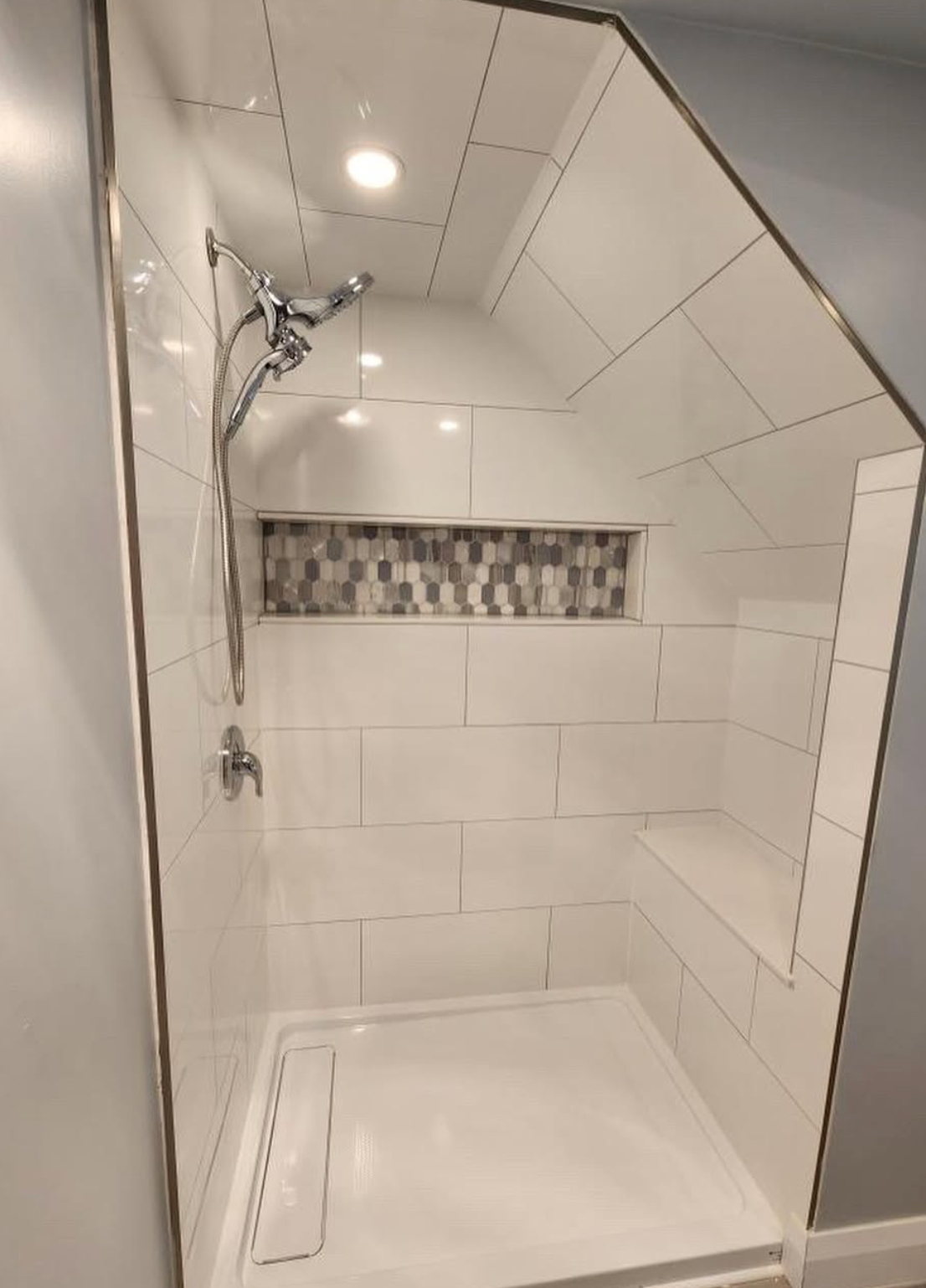 Tiled walk-in shower with rainfall showerhead, built-in bench, and decorative mosaic accent strip.