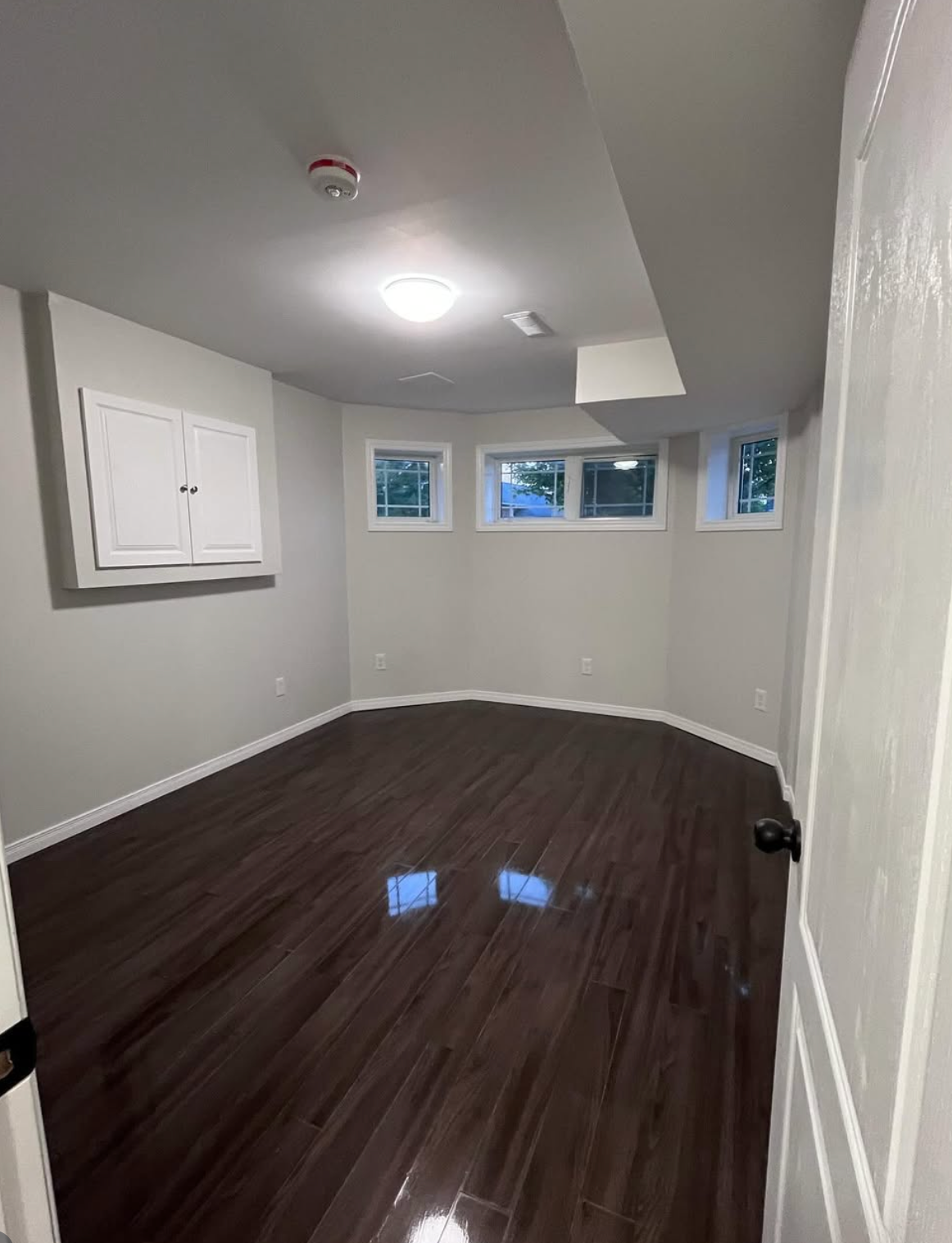 Empty gray room with dark wood floor, white trim, and small windows on the far wall.
