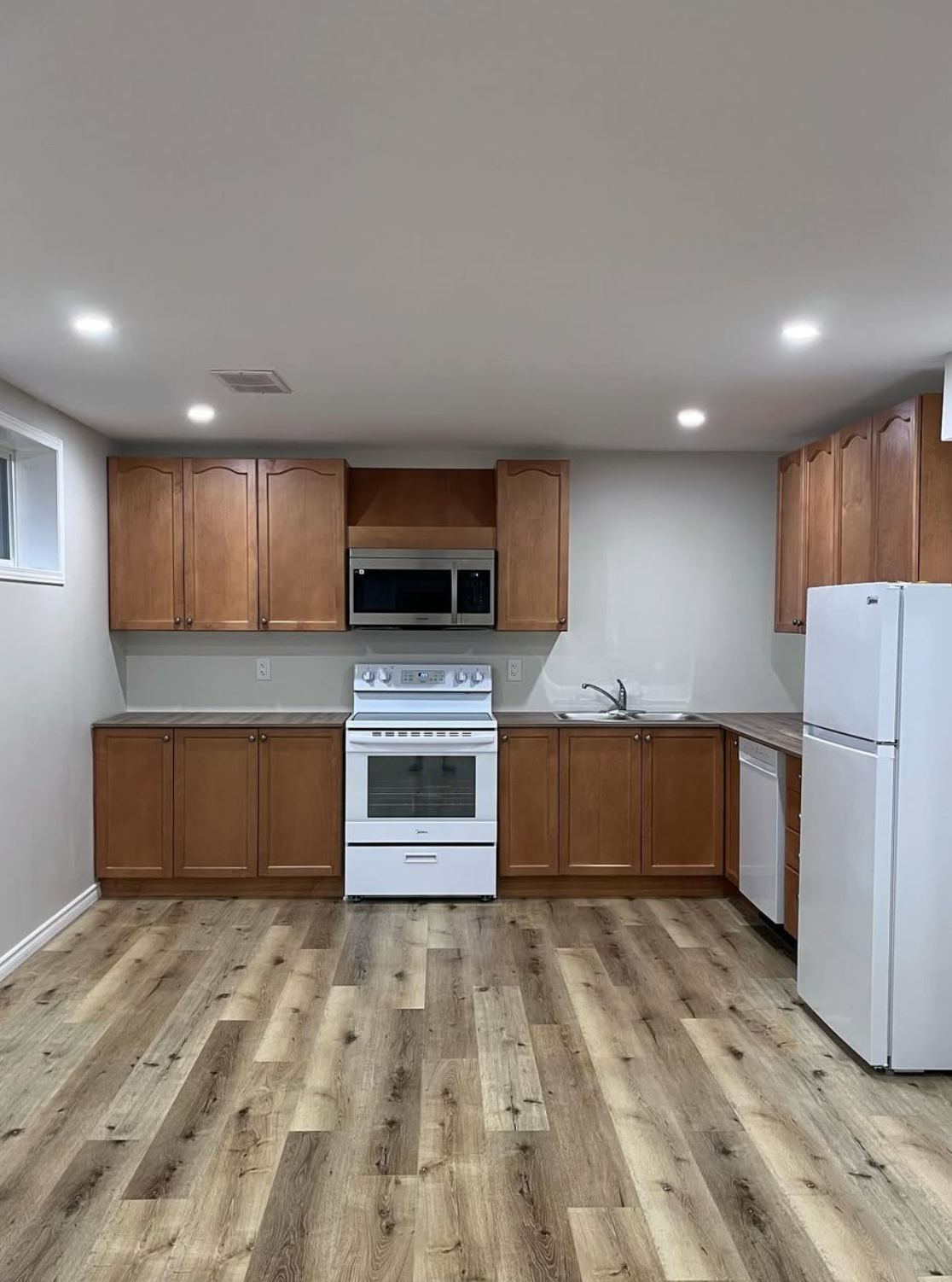 Small kitchen with wooden cabinets, white appliances, and light wood flooring.