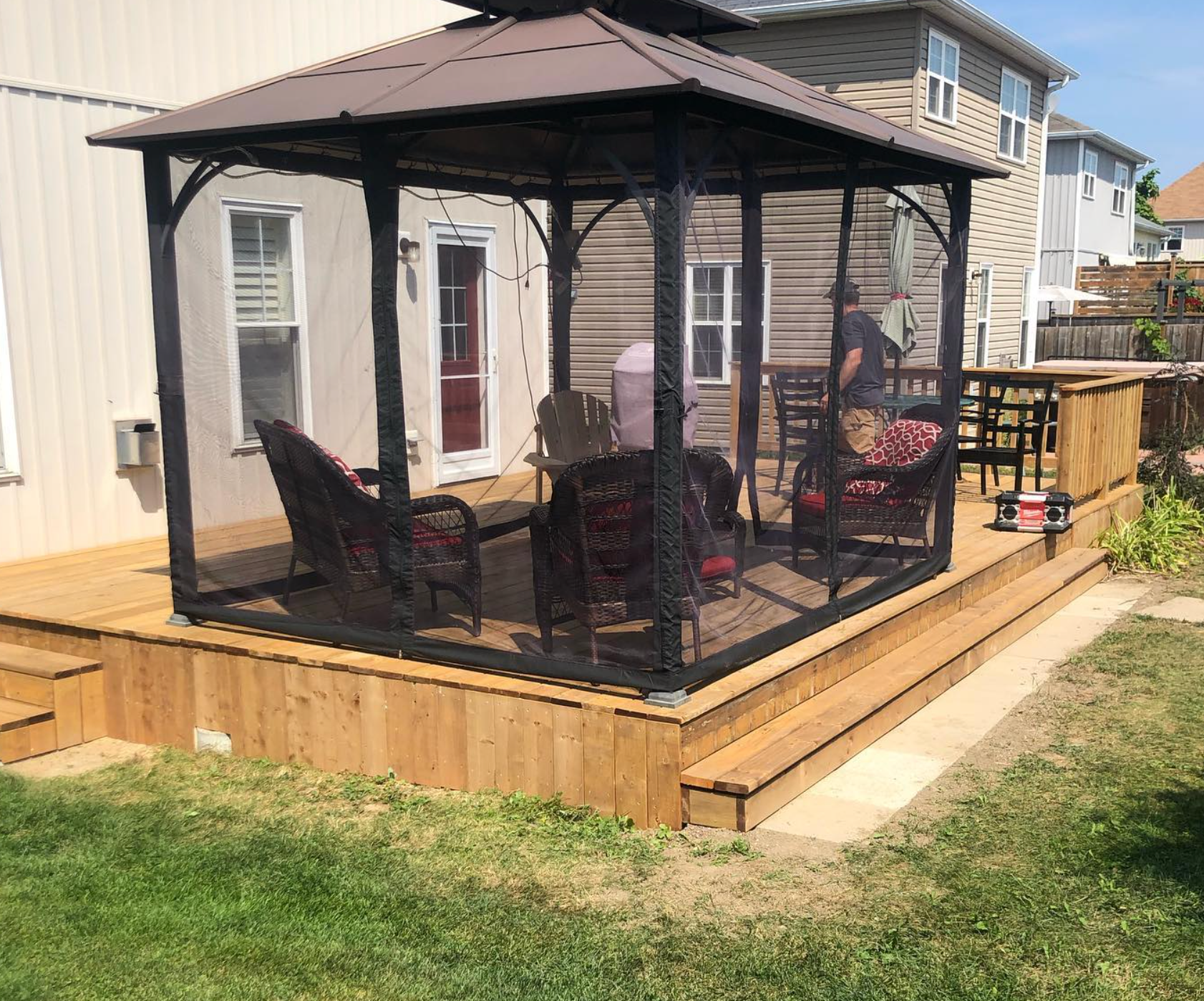 Black metal gazebo on a wooden deck in a backyard with chairs and a small table