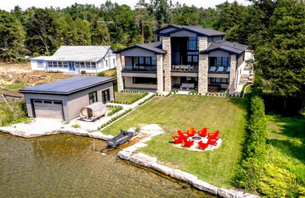 Kawartha Lakes modern house with dock, boathouse, and red chairs on a grassy waterfront lawn