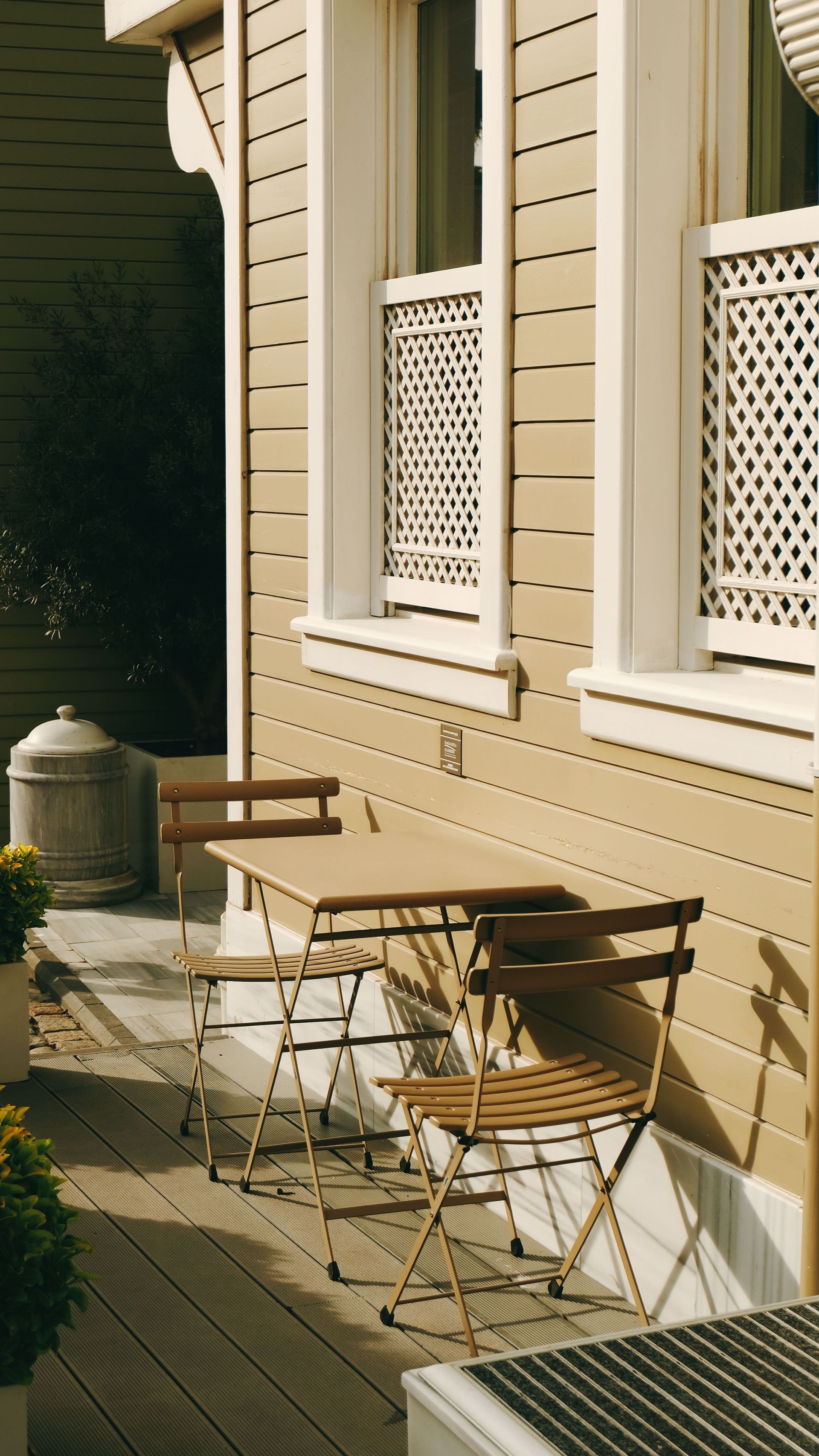 Sunlit beige townhouse exterior with small patio chairs and white-trimmed windows