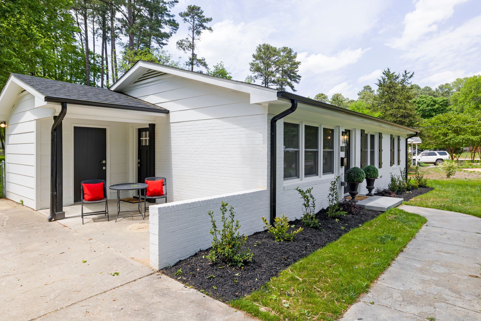 White single-story house with front porch, red chairs, and landscaped walkway beside driveway