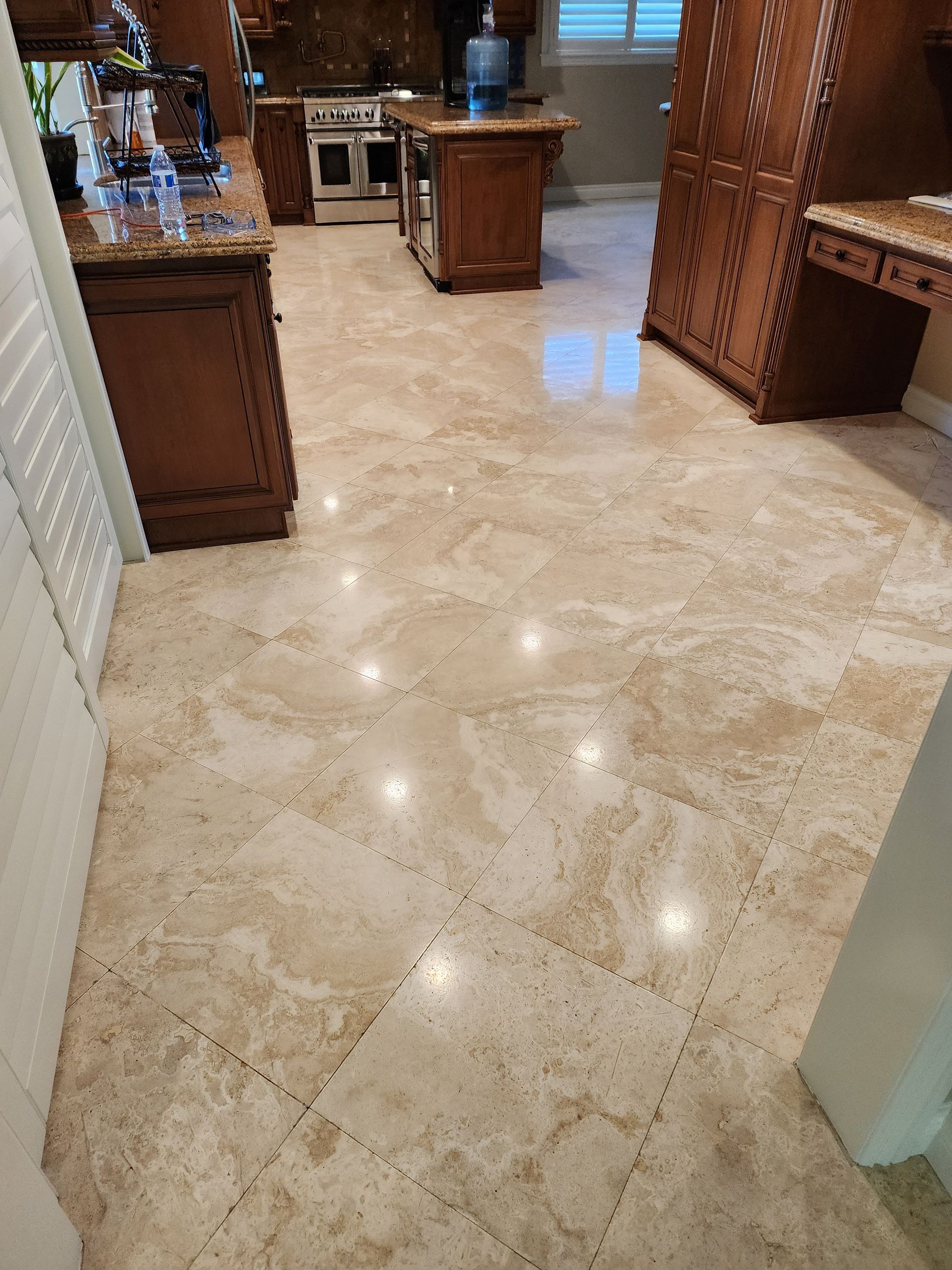 Beige tile floor in a kitchen with dark wood cabinets and a central island; overhead lighting causes reflections.