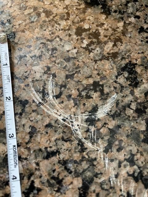 Scratches on a granite countertop, partially visible with a measuring tape in the frame.