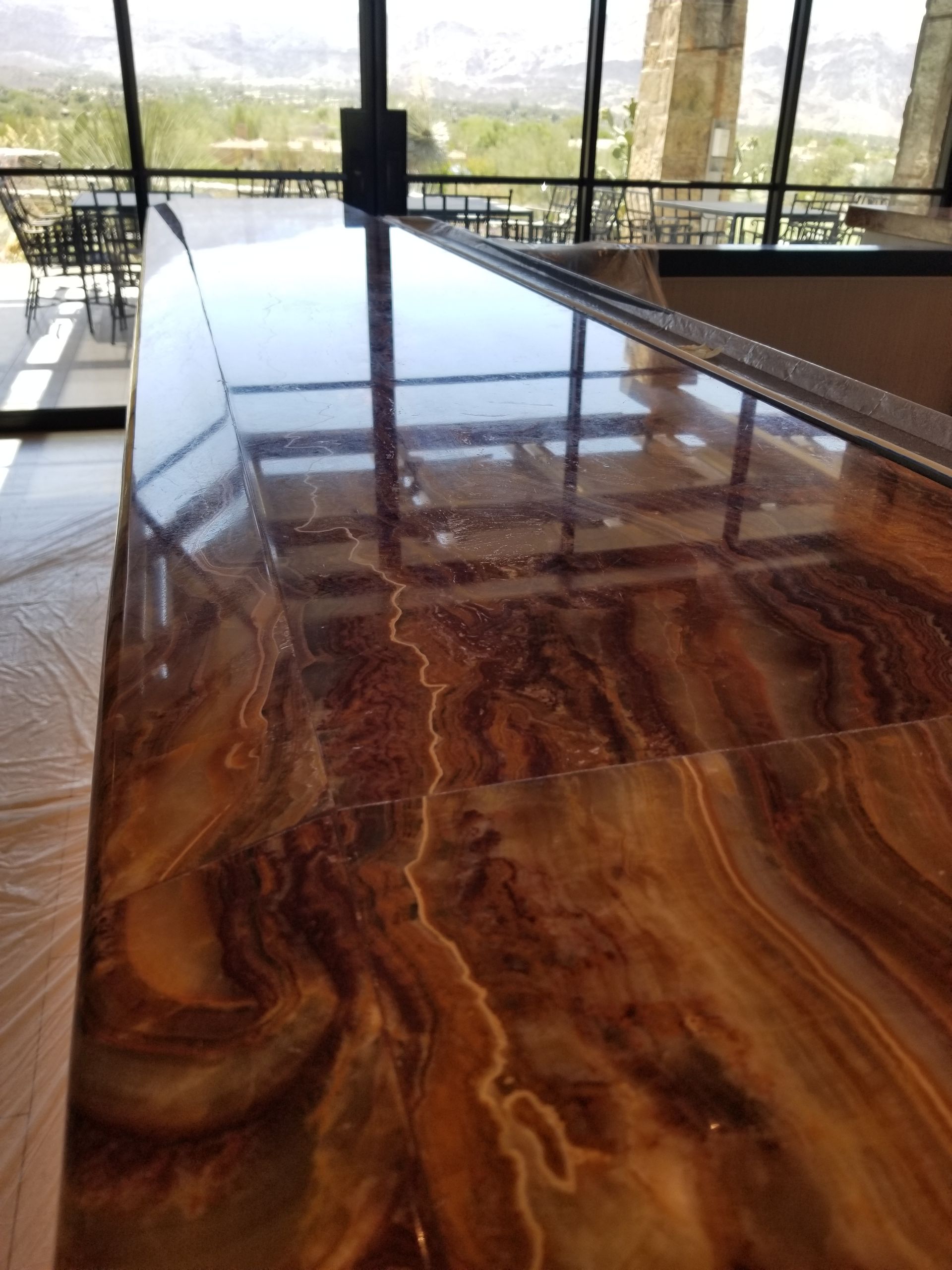 Glossy, brown-toned countertop with marbled patterns, reflecting a window view.