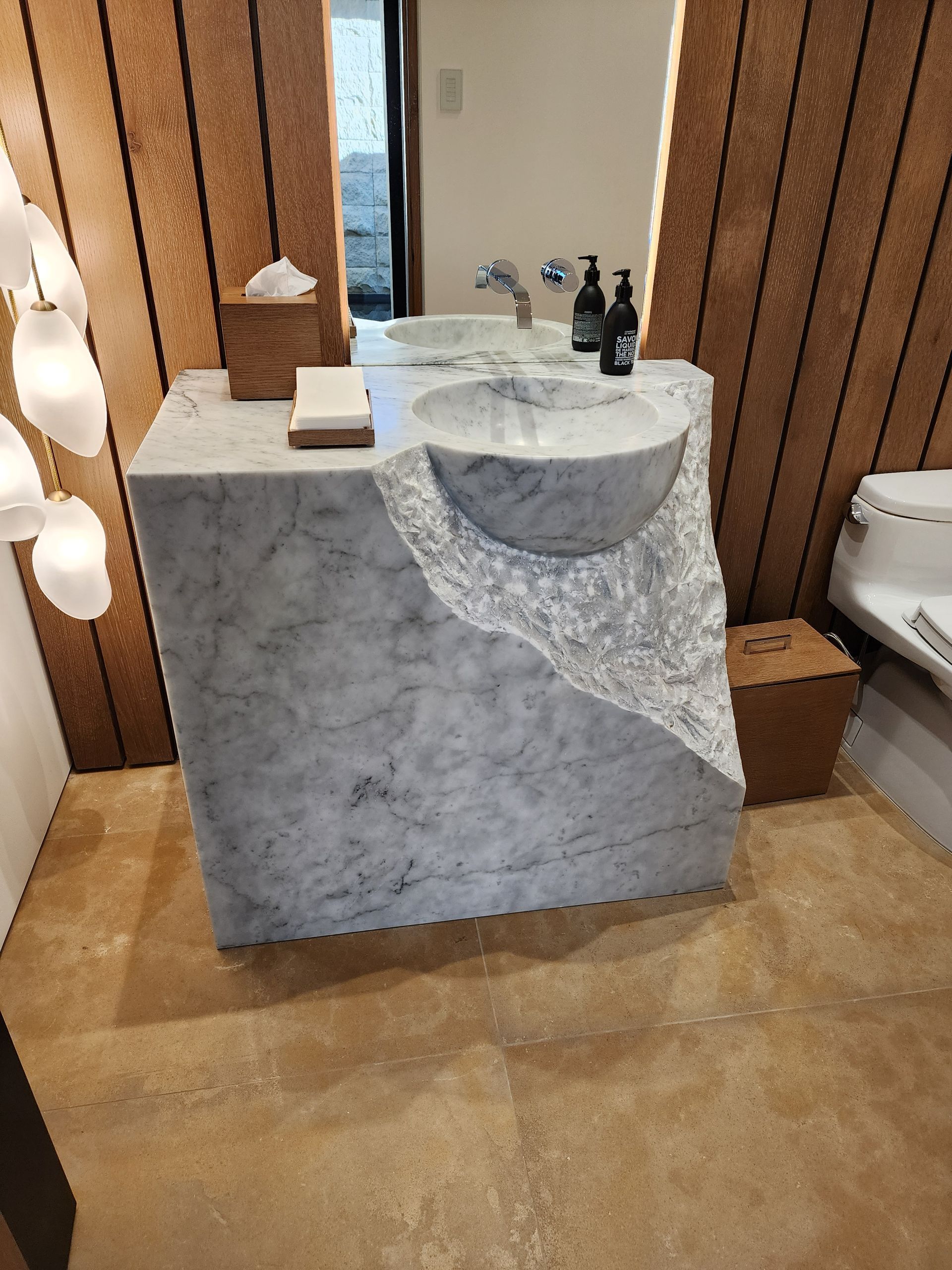 Marble bathroom sink with irregular carved front, two basins, and a mirror.