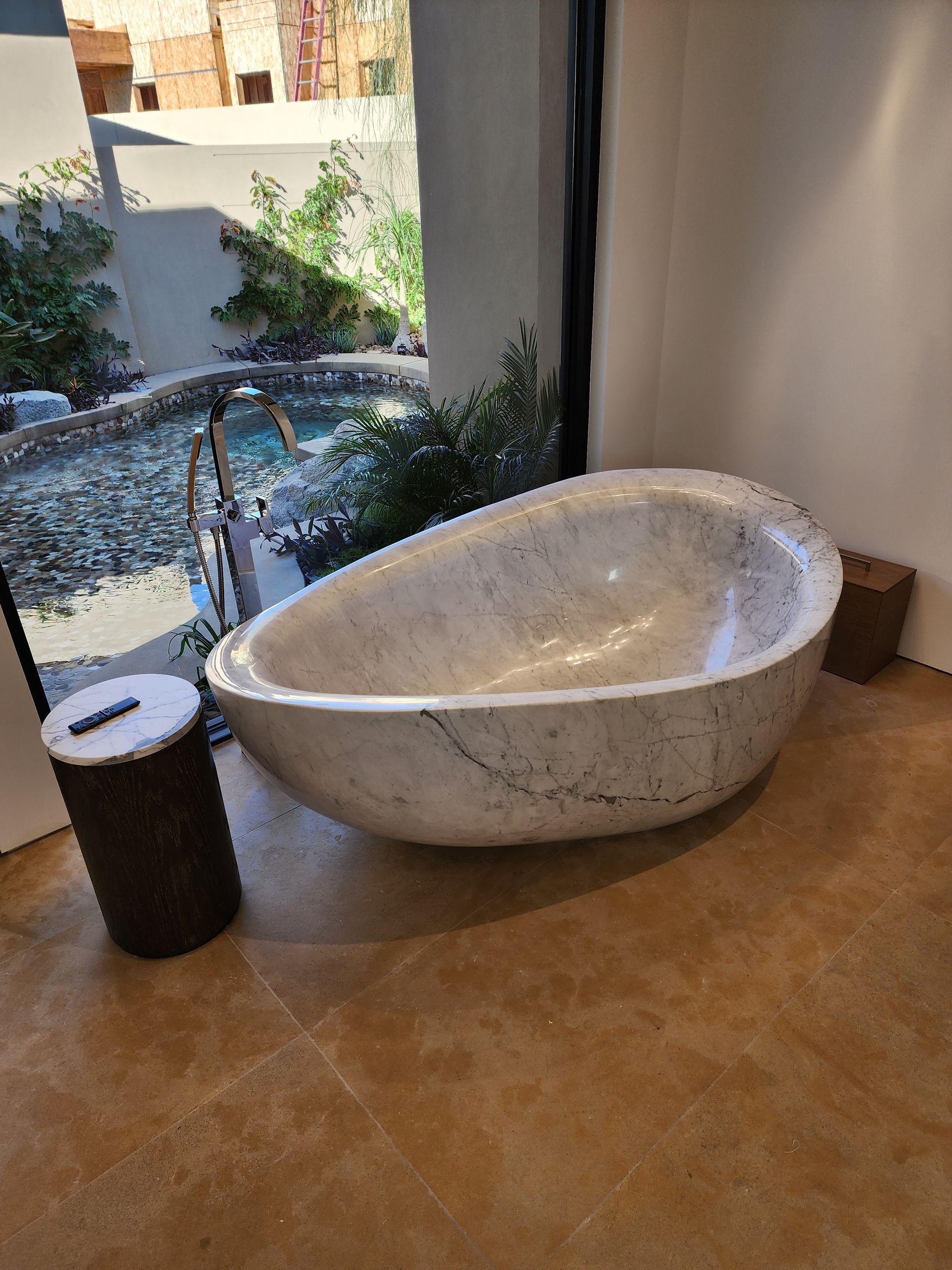 Oval marble bathtub next to a window overlooking a water feature.