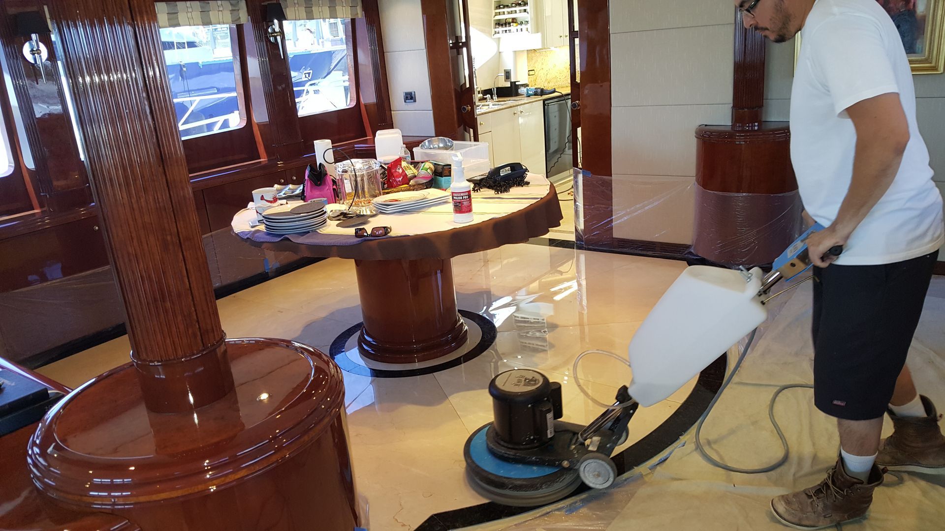 Man cleans a shiny floor with a floor buffer on a yacht with a wooden interior.