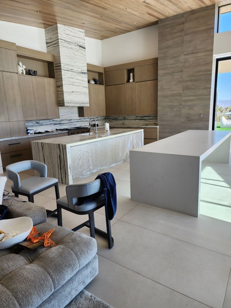 Modern kitchen with two islands, cabinetry, and seating. Neutral tones and natural light.