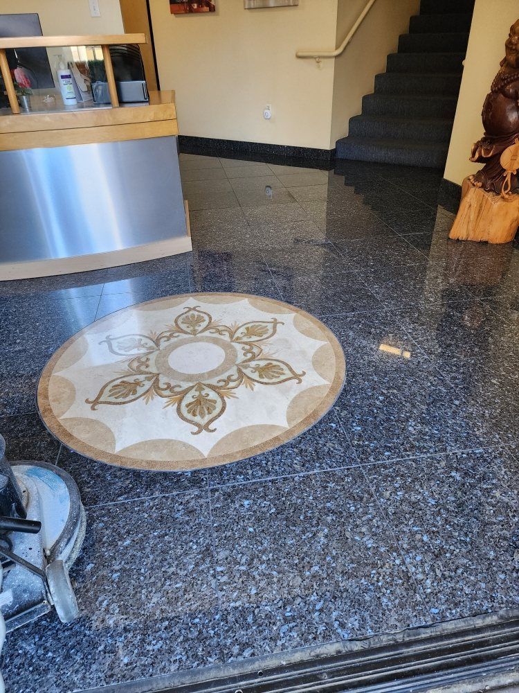 Circular decorative floor inlay in a lobby with dark flooring, near a stairway and a desk.