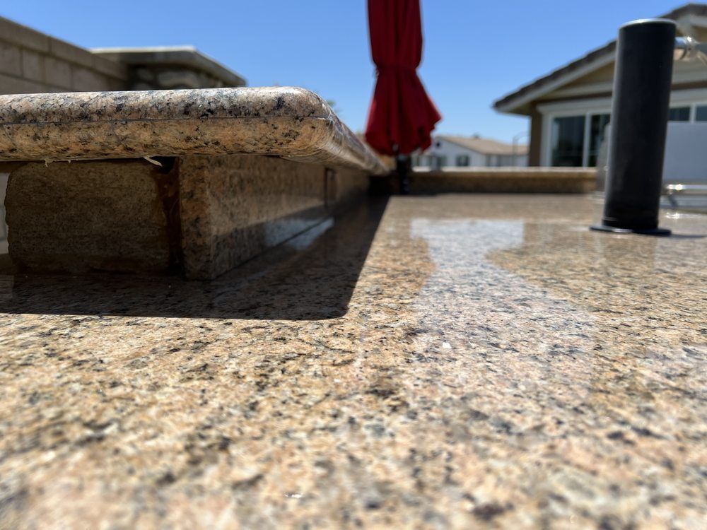 Close-up of a light granite surface with a red umbrella in the background. Sunny day.