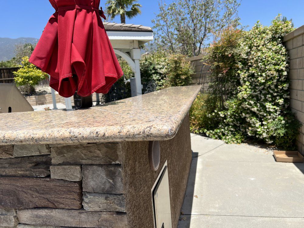 Outdoor kitchen counter with granite top, stone base, and red umbrella.