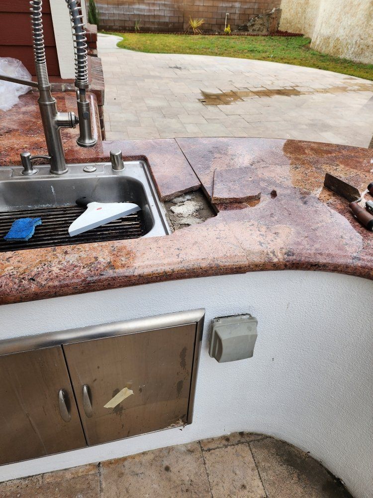 Outdoor kitchen with granite countertop, a damaged area, stainless steel sink, and cabinets.