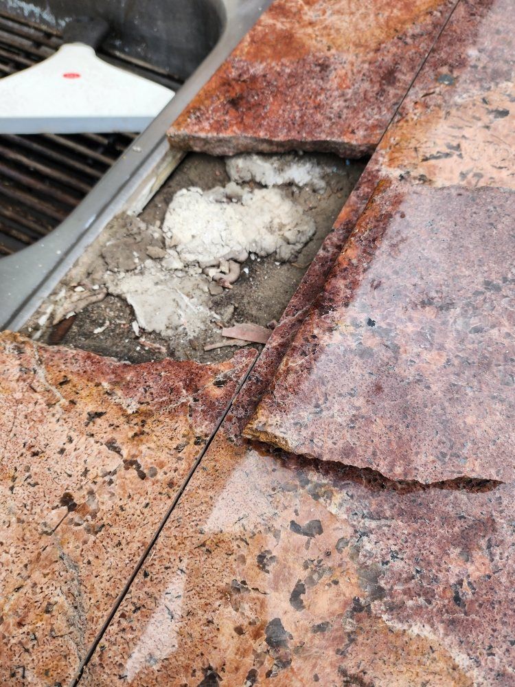 Damaged stone tiles on a surface, revealing crumbling mortar and a white, powdery substance.