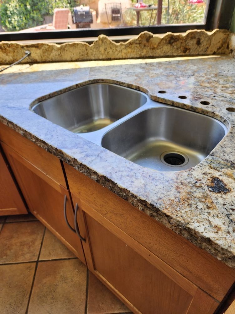 Stainless steel double sink in a granite countertop over wood cabinets.