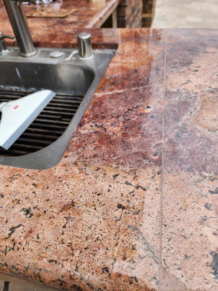 Close-up of a granite countertop with a built-in sink. The granite is red-brown with black flecks.