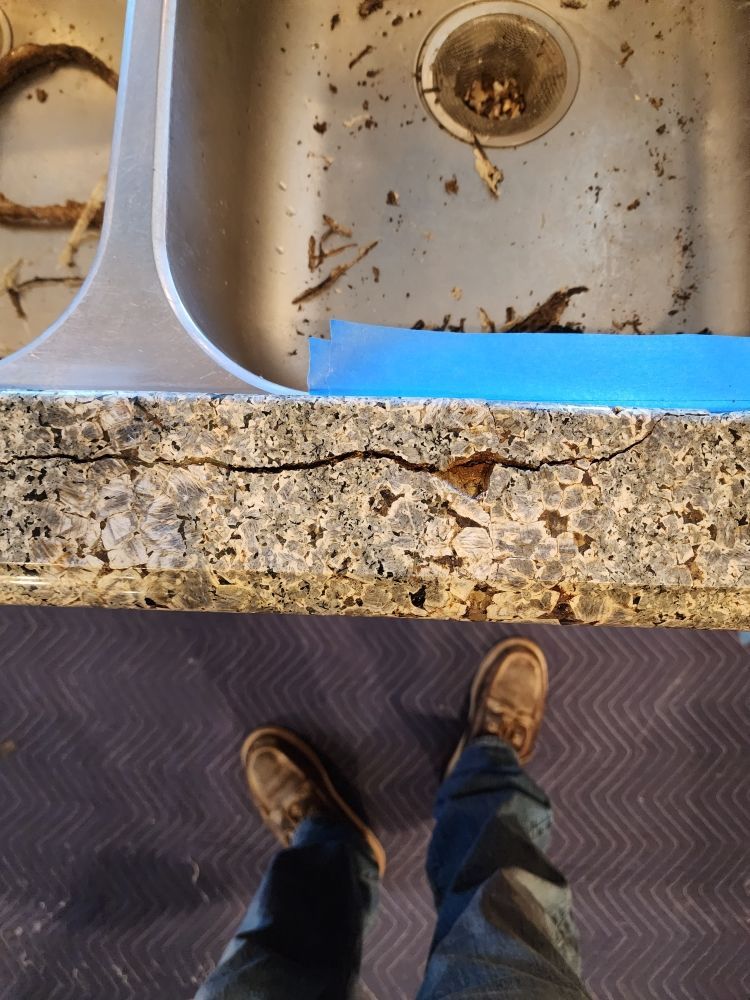 Person standing in front of a cracked countertop near a dirty sink.