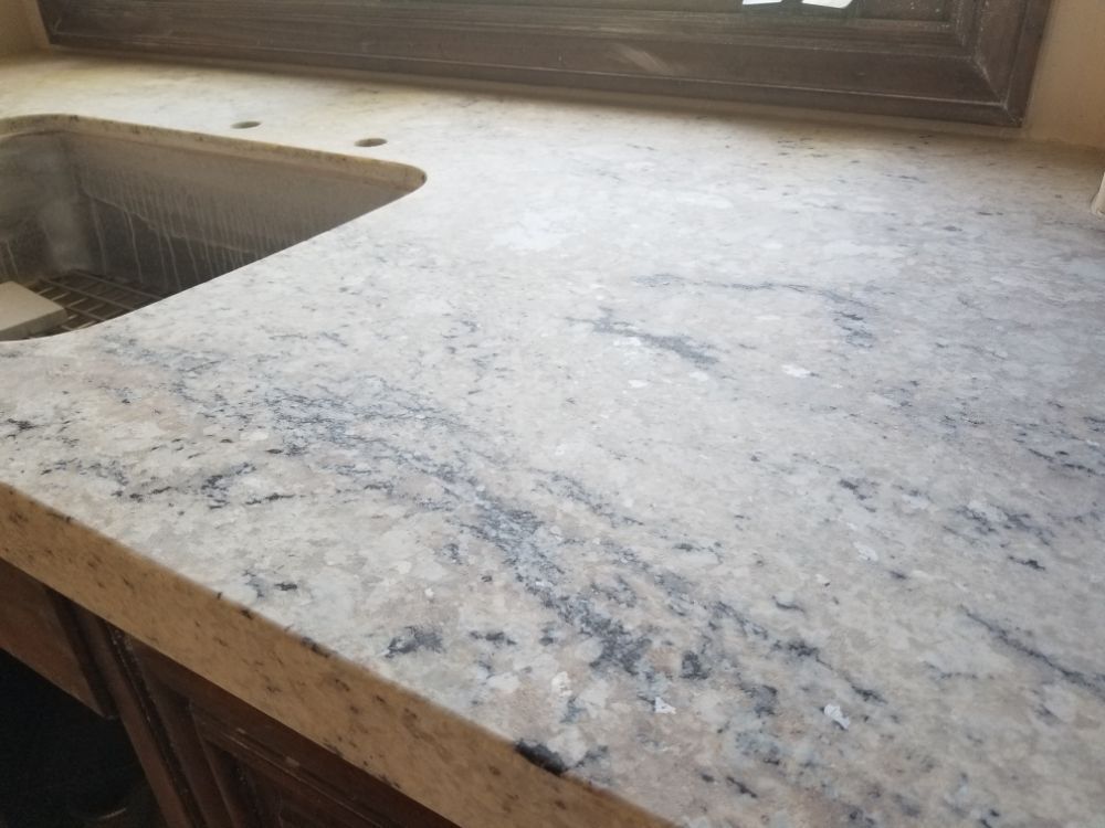 Cream-colored granite countertop with dark blue veins, over a wooden cabinet, and a rectangular sink.