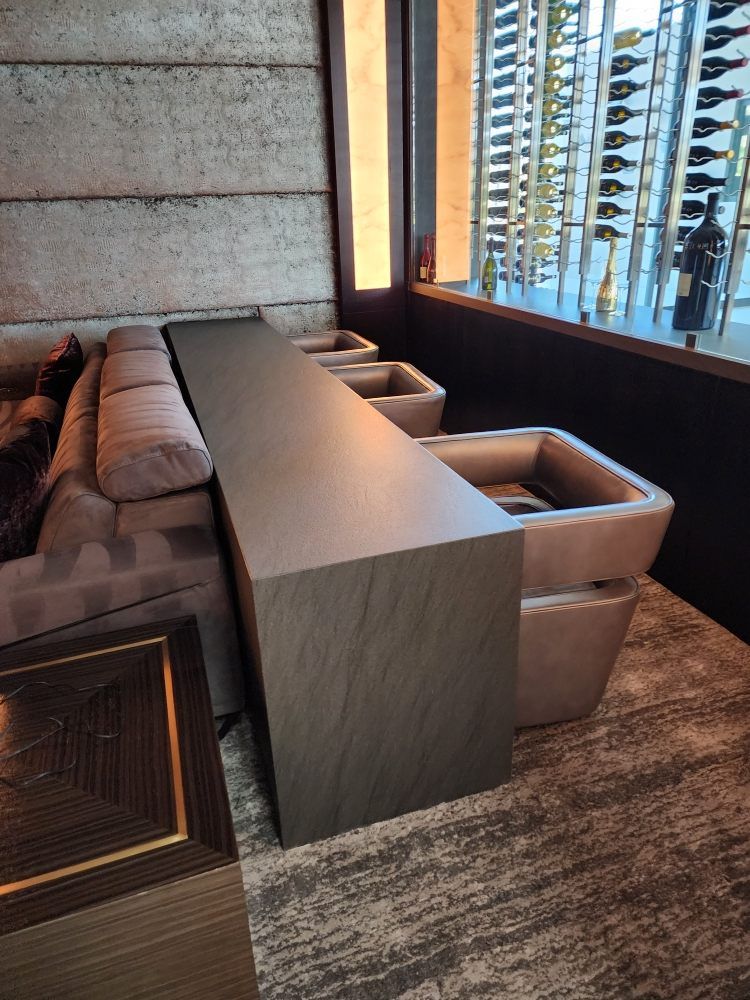 A modern lounge area with a sofa, armchairs, and a wine rack visible through the window.