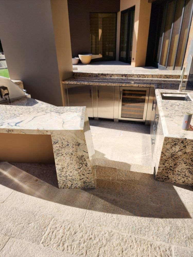 Outdoor kitchen with granite counters, stainless steel appliances, and stone patio.