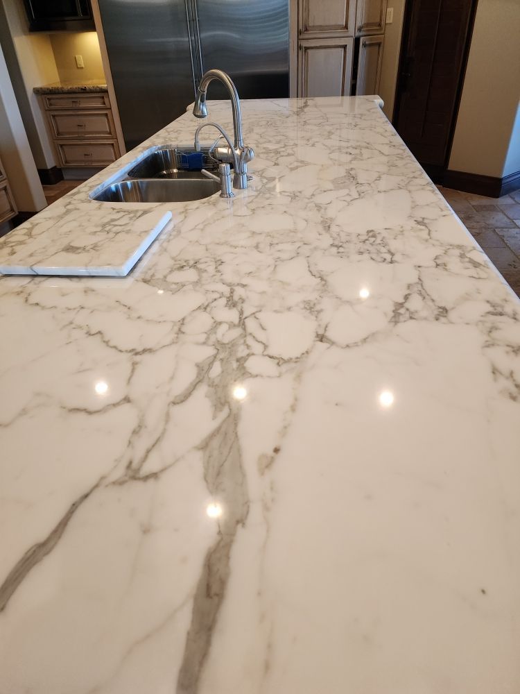 White marble countertop with gray veining, a sink, and faucet in a kitchen.