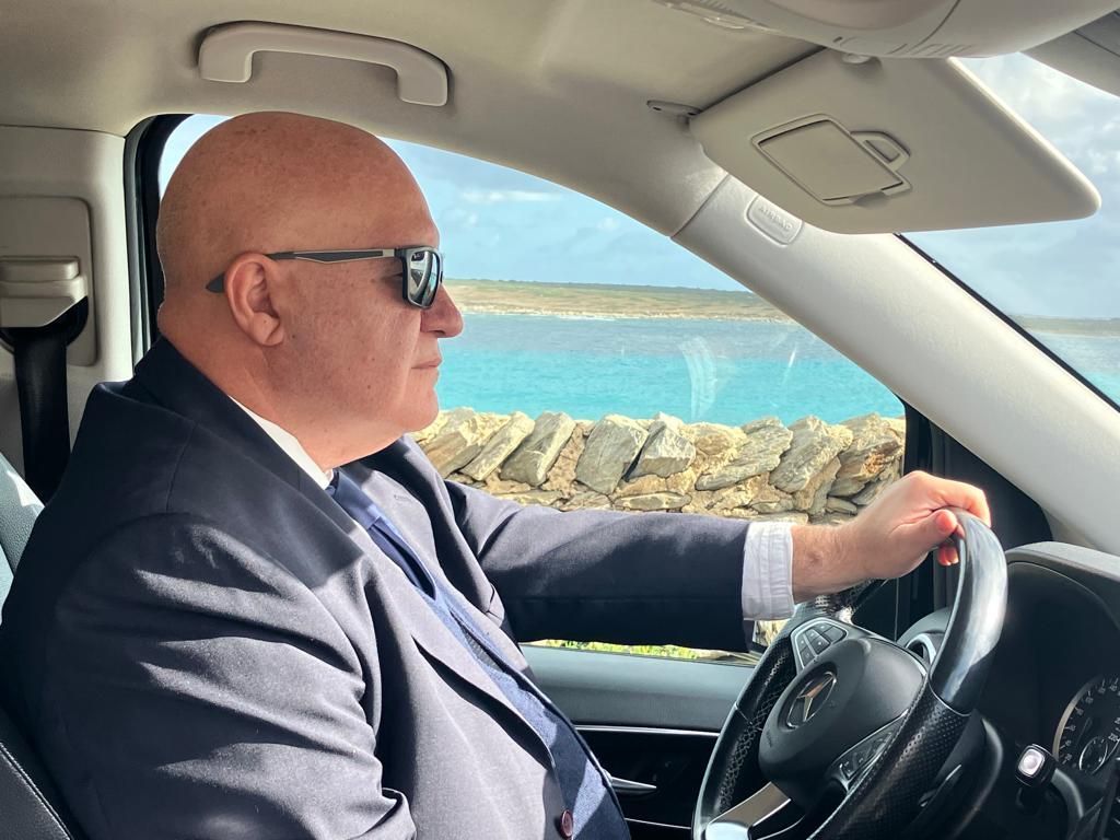 un uomo che indossa un abito e occhiali da sole guida un'auto